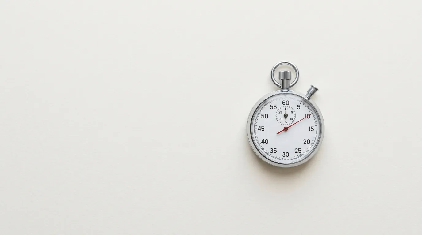 A plain chrome stopwatch lying on an off-white surface, its red hand stopped just past the top